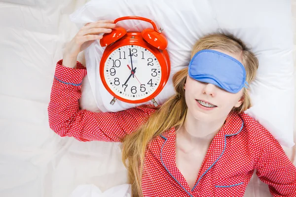 Sovande kvinna klädd i pyjamas håller klockan — Stockfoto