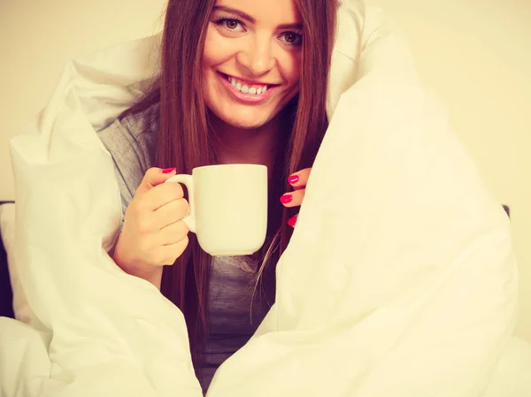 Mujer sonriente sosteniendo una taza de bebida en la cama —  Fotos de Stock