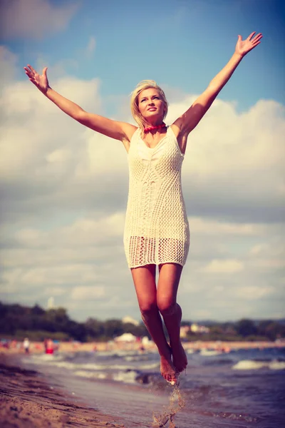 Mulher loira vestindo vestido jogando salto na praia — Fotografia de Stock