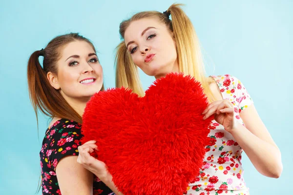 Happy two women holding heart shaped pillow — Stock Photo, Image