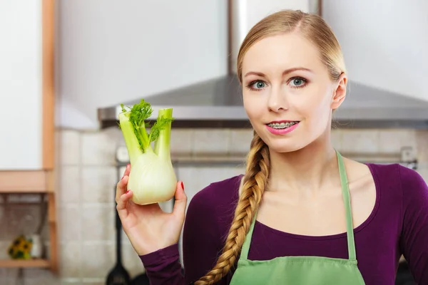 Woman in kitchen holds raw fennel bulb vegetable