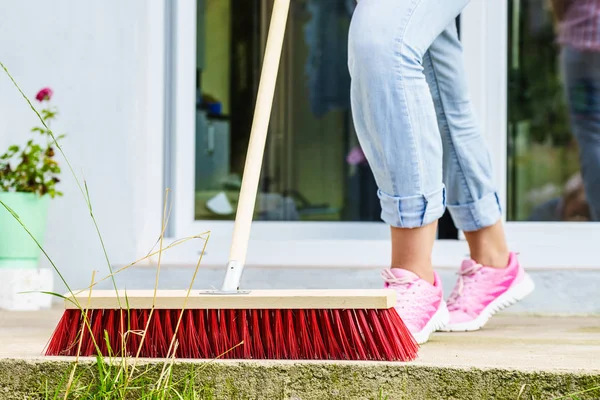 Woman using broom to clean up backyard patio — Stock Photo, Image