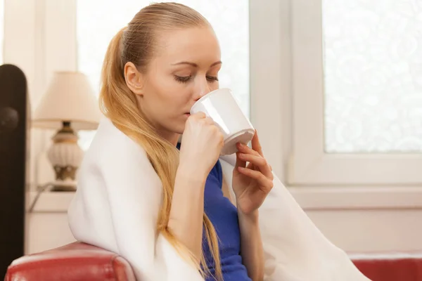 Mujer acostada en un sofá bajo una manta bebiendo té —  Fotos de Stock