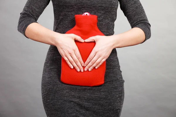 Girl holds hot water bottle on belly making heart shape by hands — Stock Photo, Image