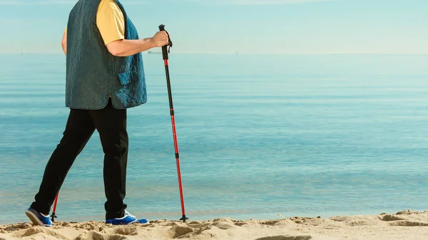 Старшая женщина занимается нордической ходьбой по пляжу — стоковое фото