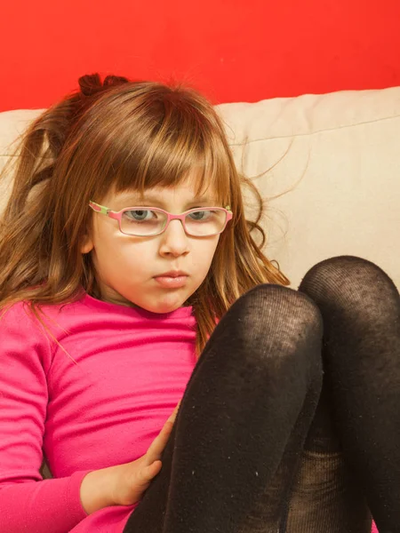 Νήπια κορίτσι με τα γυαλιά, κάθεται στον καναπέ — Φωτογραφία Αρχείου
