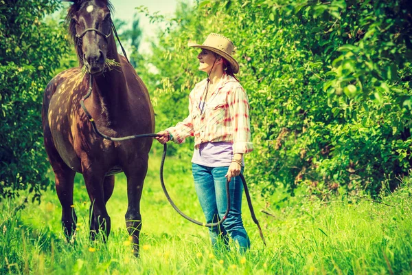 Západní žena chůze na zelenou louku s koněm — Stock fotografie