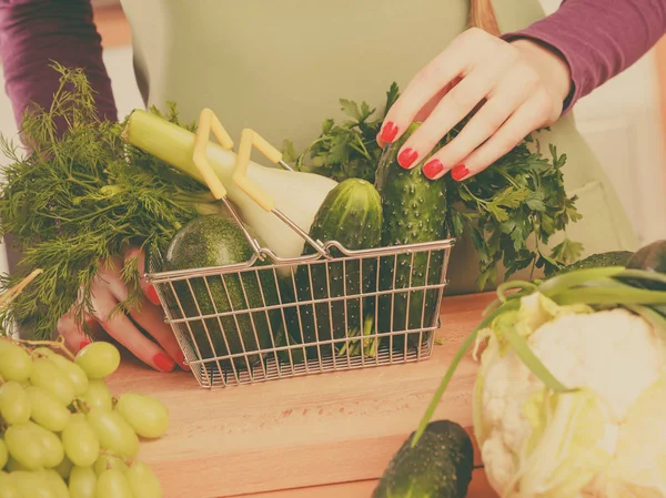 Kvinna i köket med grönsaker håller varukorg — Stockfoto