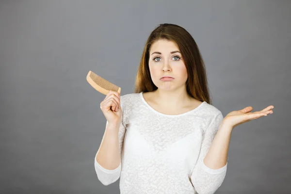 Atractiva joven mujer siendo confundida sosteniendo peine — Foto de Stock