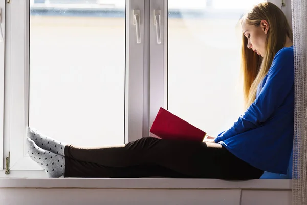 Woman sitting on window sill reading book at home — Stock Photo, Image
