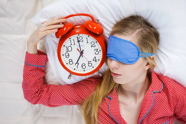 Schlafende Frau im Schlafanzug hält Uhr — Stockfoto