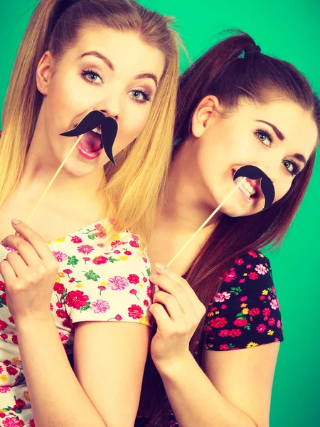 Dos mujeres felices sosteniendo bigote falso en palo — Foto de Stock