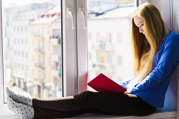 Woman sitting on window sill reading book at home — Stock Photo, Image