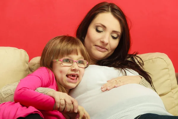 Femeie însărcinată care stă pe canapea cu fiica — Fotografie, imagine de stoc