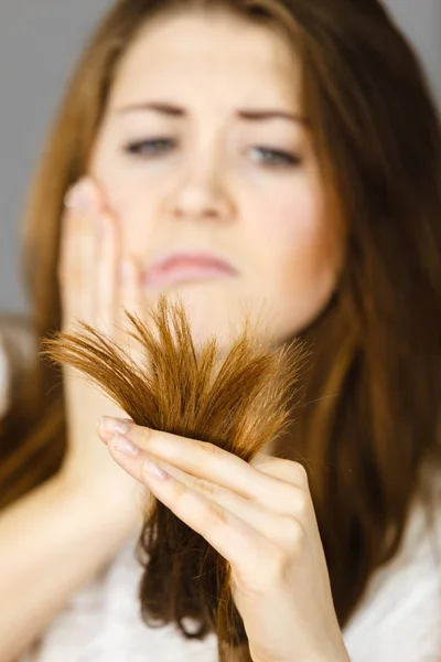 Worried woman looking at her dry hair ends — Stock Photo, Image