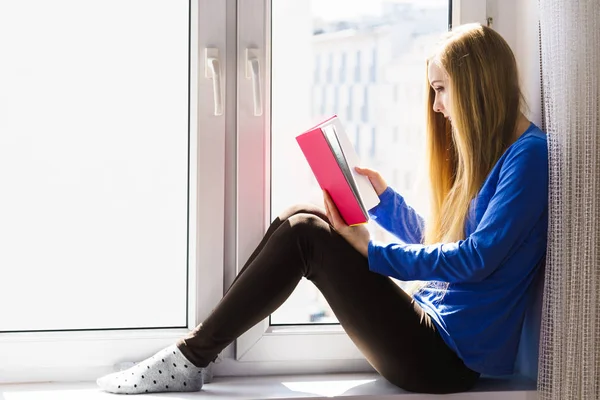 家で本を読んでの窓枠に座っている女性 — ストック写真
