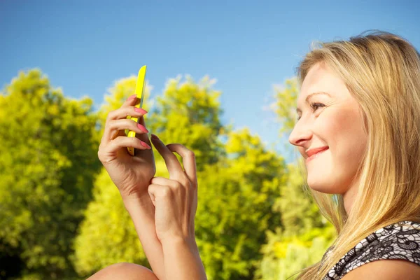 Woman sitting in park, using phone taking pictures — Stock Photo, Image