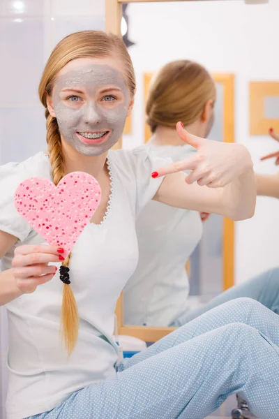 Mujer con máscara facial gris sosteniendo esponja de corazón — Foto de Stock