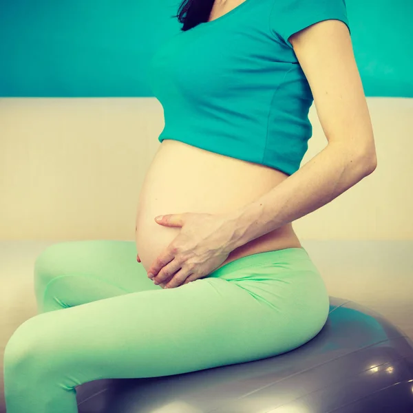 Femeie gravidă care stă pe mingea de potrivire, atingând burta — Fotografie, imagine de stoc