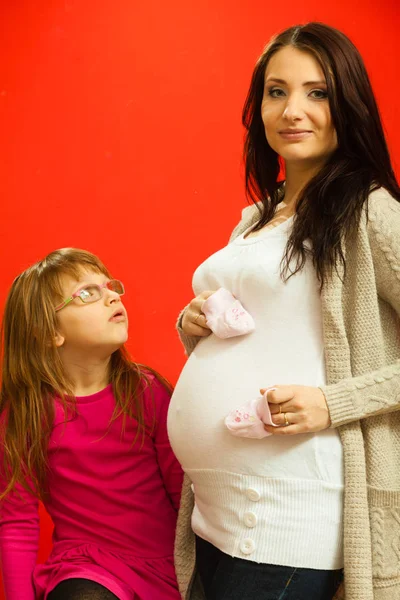 Mujer embarazada con niña pequeña sosteniendo zapatos de bebé — Foto de Stock