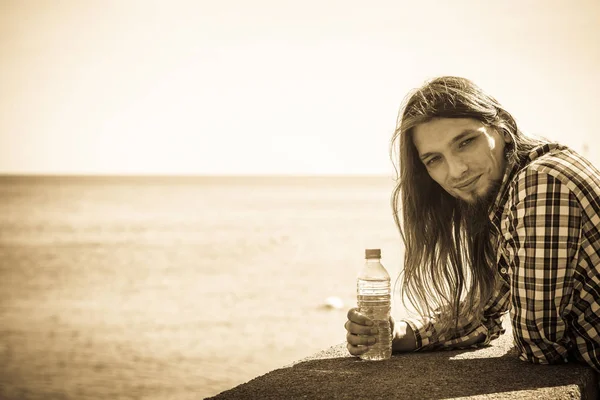 Mann mit langen Haaren entspannt am Meer Wasser trinken — Stockfoto