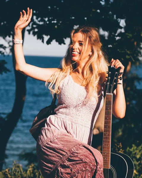 Blonde vrouw met akoestische gitaar aan zee — Stockfoto