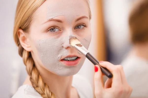 Frau trägt mit Pinsel Lehmmaske auf ihr Gesicht auf — Stockfoto