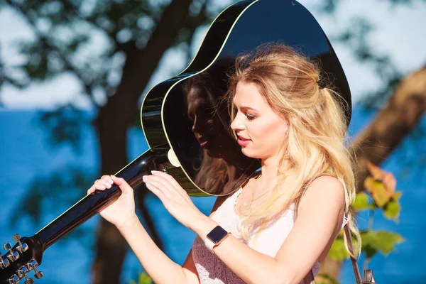 Blonde vrouw met akoestische gitaar aan zee — Stockfoto