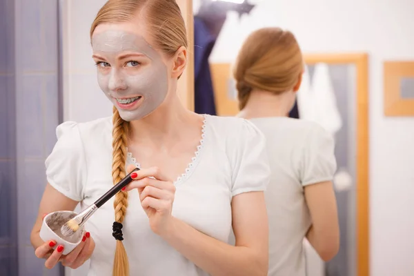 Mujer joven feliz aplicando máscara de barro en la cara — Foto de Stock