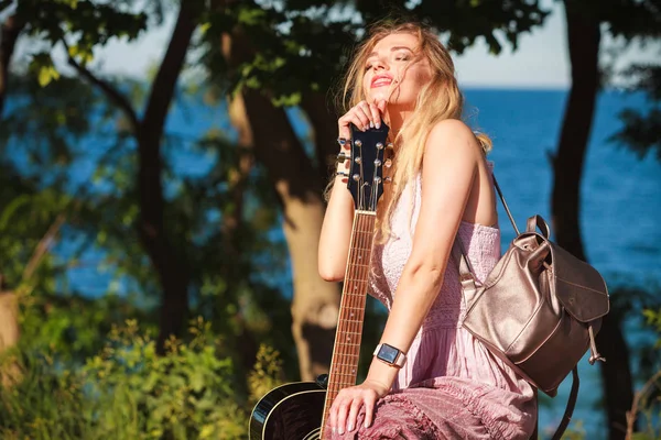 Blonde vrouw met akoestische gitaar aan zee — Stockfoto