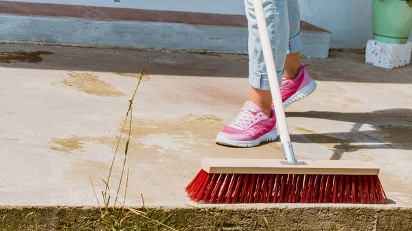 Woman using broom to clean up backyard patio — Stock Photo, Image