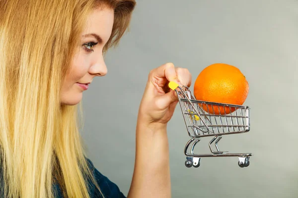 Mujer sosteniendo carrito de compras con naranja en el interior — Foto de Stock