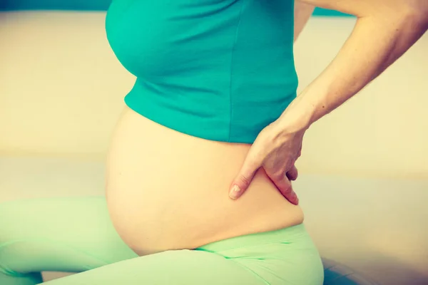 Femme enceinte assise sur le canapé tient la main sur le dos — Photo