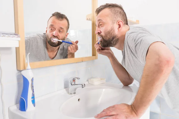 Ένας Ενήλικας Βουρτσίζει Δόντια Του Κοιτάζοντας Τον Καθρέφτη Του Μπάνιου — Φωτογραφία Αρχείου