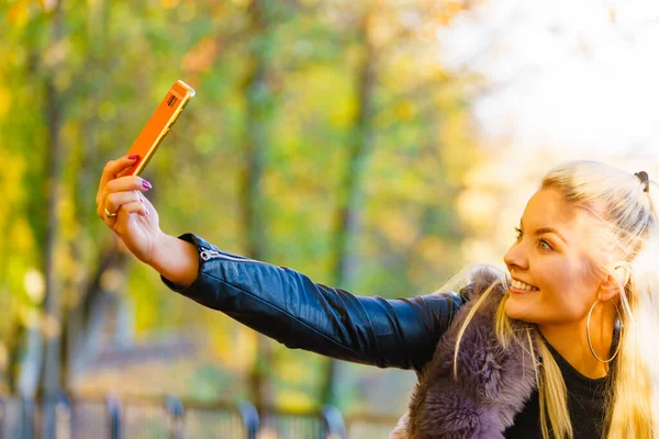 金发迷人的女人穿着时髦的服饰 精致的毛皮外套 走在秋天的公园里 用智能手机拍着自拍 快乐而积极的女性 — 图库照片