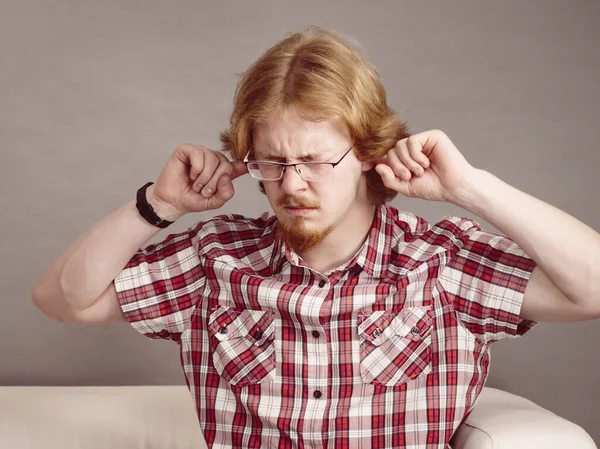 Man being annoyed with loud noise having fingers in ears pretending to be deaf