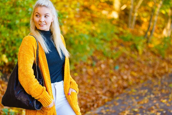 穿着时髦衣服的女人穿着黄色羊毛衫在秋天的公园里散步 — 图库照片