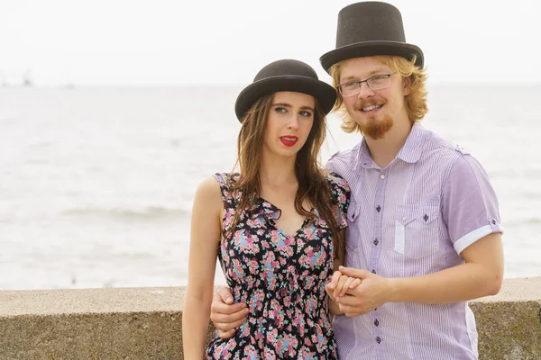 Vintage retro couple, man and woman enjoying their romantic date outside wearing fedora hats by seaside