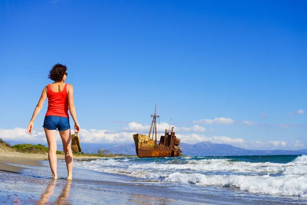 旅の自由 夏休みを楽しむビーチを歩く熟女観光客の女性 古い放棄された難破船 バックグラウンドで難破船 — ストック写真