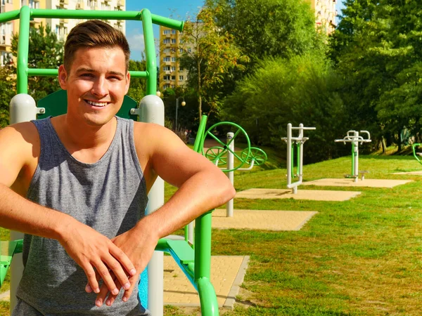 Sportsman relaxing after outdoor workout at street exercise machines for strength exercises. Fit man feeling healthy enjoying sun