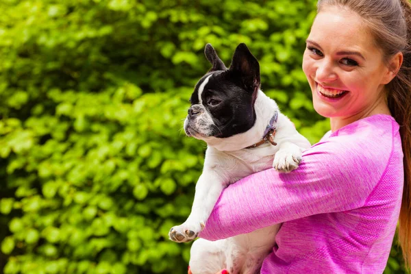 動物の恋人 小さなペット 犬の楽しいコンセプト 外の公園で小さなかわいいフランスのブルドッグを保持するスポーツ服を着て幸せな笑顔の女性 — ストック写真