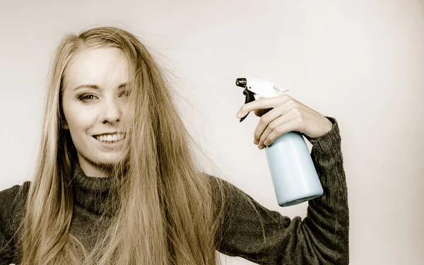 Girl messy long dry hair holding bottle, applying thermal protect hair spray.