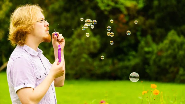 幸せな若いです大人男吹いて石鹸泡で自然緑の春公園 — ストック写真