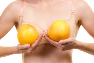 Slim young woman small boobs wearing bra holding big orange fruits. Breast enlargement size correction concept. clipart