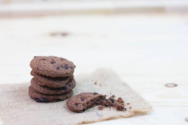 Chocolate chip cookies with a bite mark placed on a sack on a wooden table.