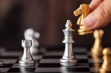 ahşap arka plan ile satranç tahtası üzerinde oyunda altın at saldırı gümüş kral tutan el