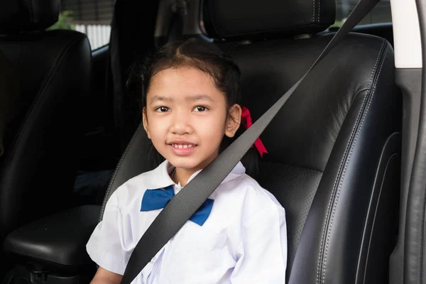 亚洲女孩穿着校服坐在车里 系好安全带 以确保安全 — 图库照片
