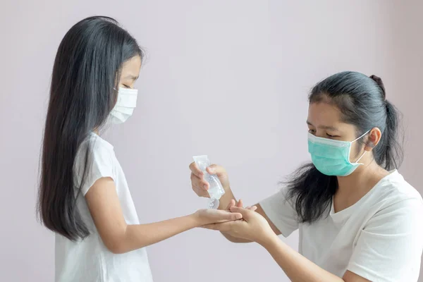 Little girl and a woman wear a protective medical mask. Hands of the mother squeeze the alcohol gel in the tube onto the palm of the daughter to clean. The protection for the Coronavirus or COVID-19.