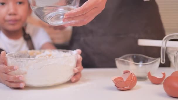 妈妈把水倒入一个混合了面粉的碗里 和一个亚洲女儿一起在碗里一起做一个自制的面包店 — 图库视频影像