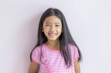 Asyalı küçük kız ışıl ışıl gülümsüyor. Pembe haç beyaz elbiseler ve uzun siyah saçlar giyen çocuklar. Çocuk ileriye bakıyor ve mutlu bir şekilde gülümsüyor. Gülen ve gülümseyen sevimli Asyalı çocuk portreleri..